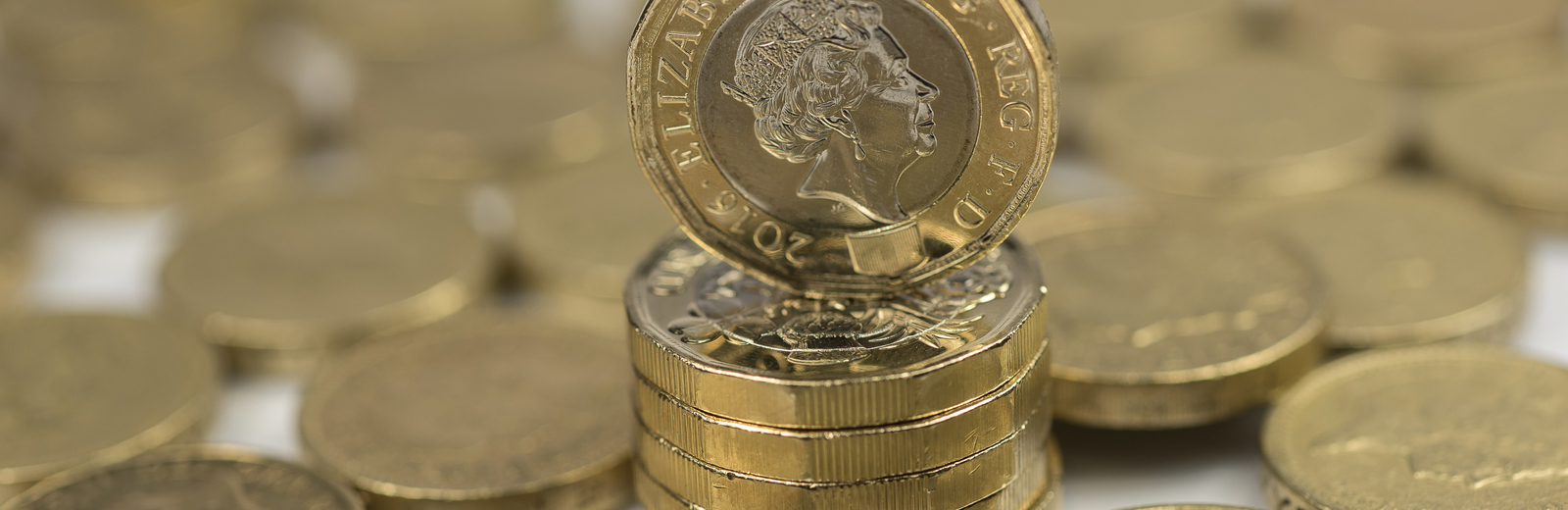 New British £1 coin on pile of old £1 coins.