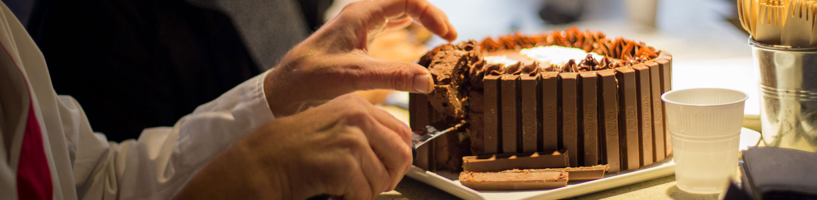 Obscured party guests cut a lice of decadent chocolate cake.