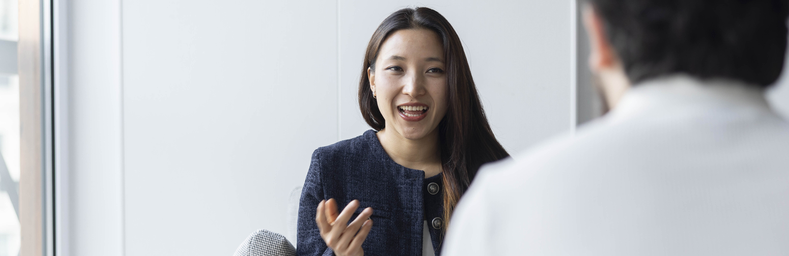 Professional young woman talking to a man out of focus opposite.