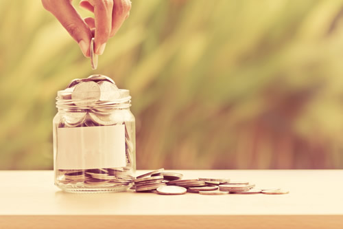 A hand adding coins to a jar