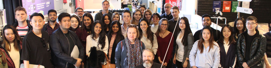 A large group of students pose for a photograph inside the Aalto Business School lobby.