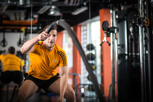A man in a gym throws heavy ropes.