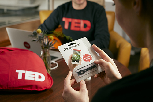 the back of a man holding a magniband, with the body of somebody wearing a TED t-shirt in the background