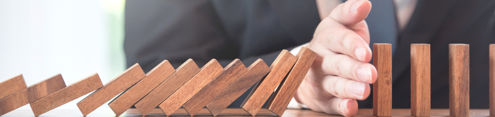 A hand prevents a domino pile from falling
