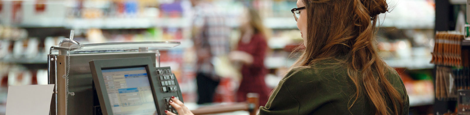 A woman sits at a cash register in a supermarket.