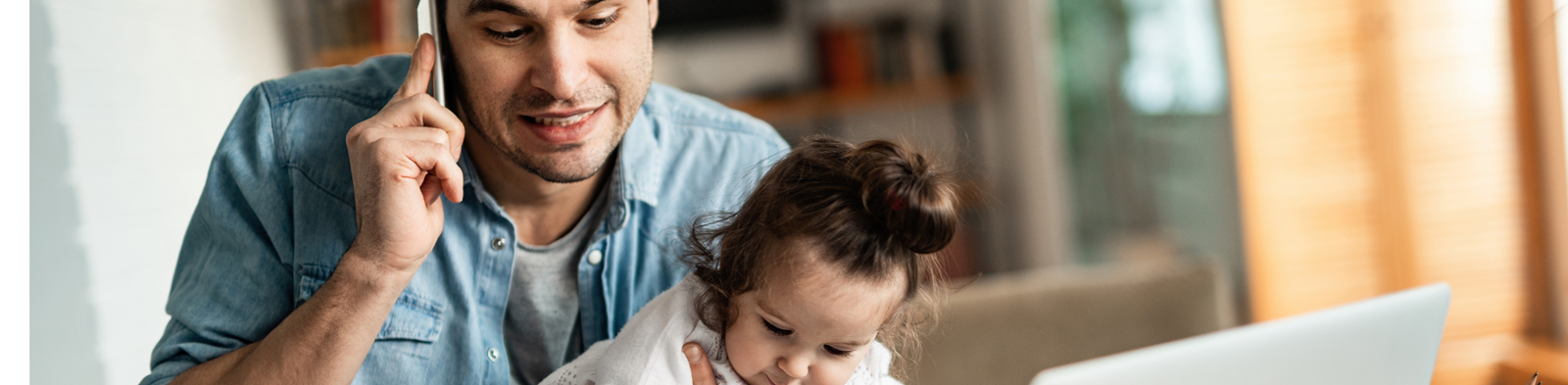 Man holding daughter while working on laptop