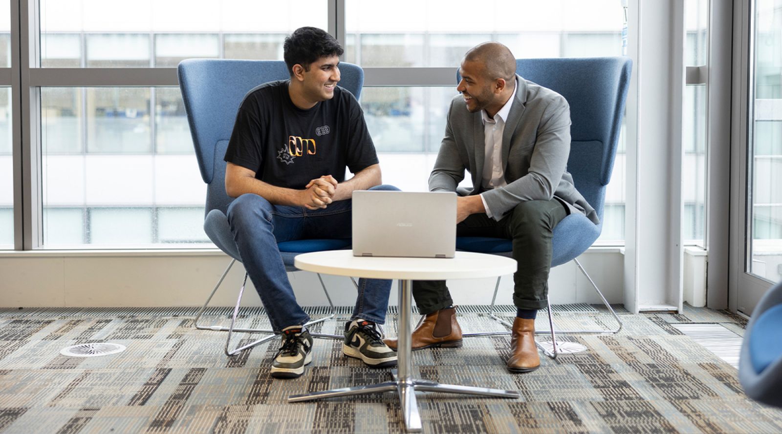 Two men sitting in chairs next to each other talking.