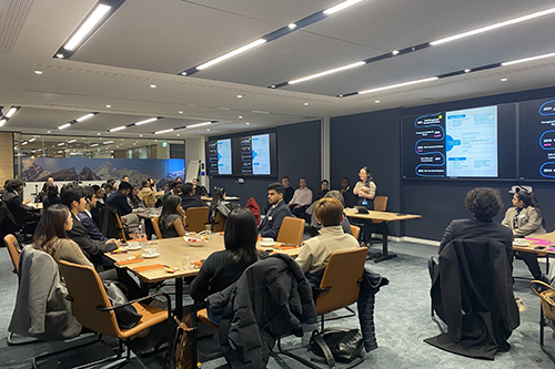 Students sitting around tables and listening to a presentation in a conference room