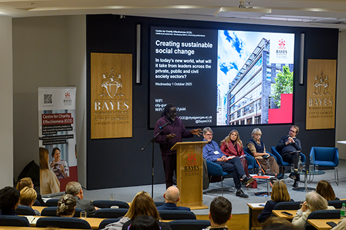 A man talks at a lectern and four people seated to his left listen.