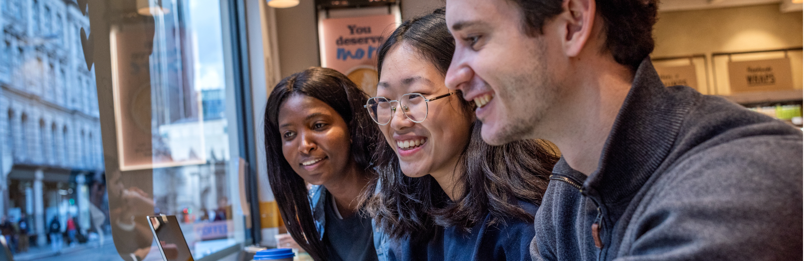 Three students looking at a laptop smiling 