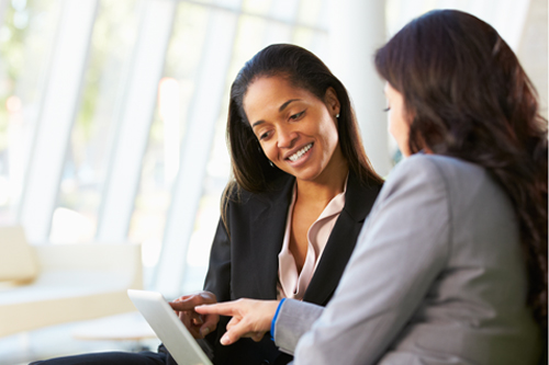 Two businesswomen looking at a laptop and talking to each other