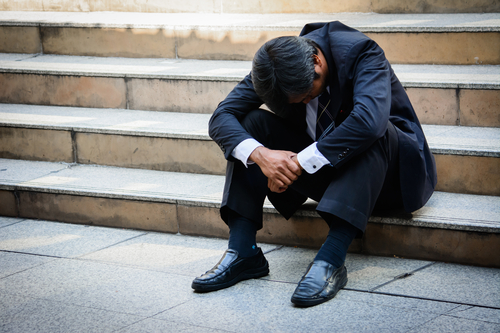 A self-employed businessman, sat on some steps, and appearing to be stressed
