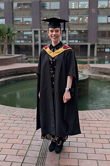 Stephanie Coughlin posing in graduation cap and gown by the pond in the Barbican Centre.
