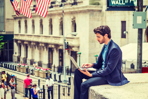 Young man in suit sitting on wall with laptop in New York. Business leaders social media