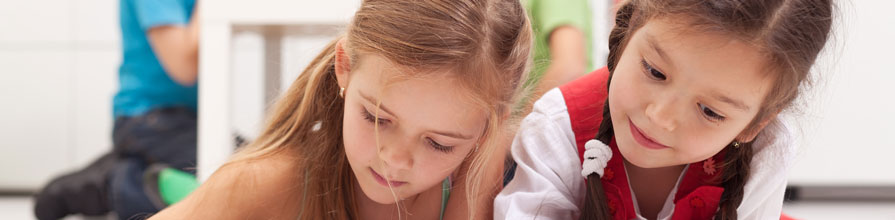 Little girls playing on a tablet computing device laying on the floor