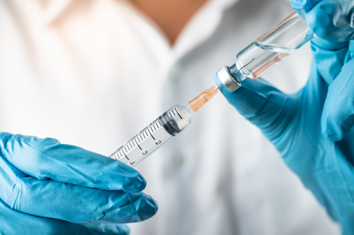 A nurse with blue gloves holding a vaccination shot