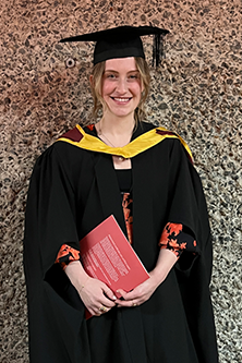 Sarah Dryden in her graduation outfit against the wall