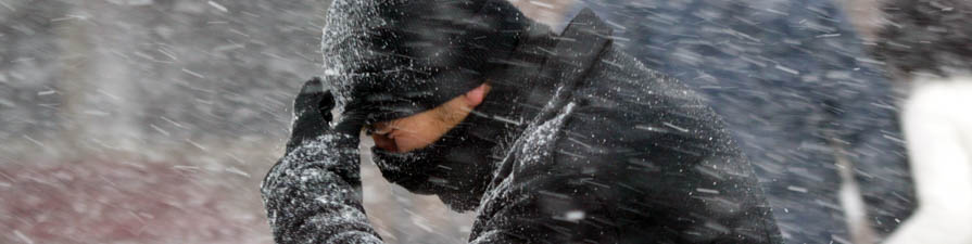 A man walks through a wild snowstorm holding a scarf to his face.