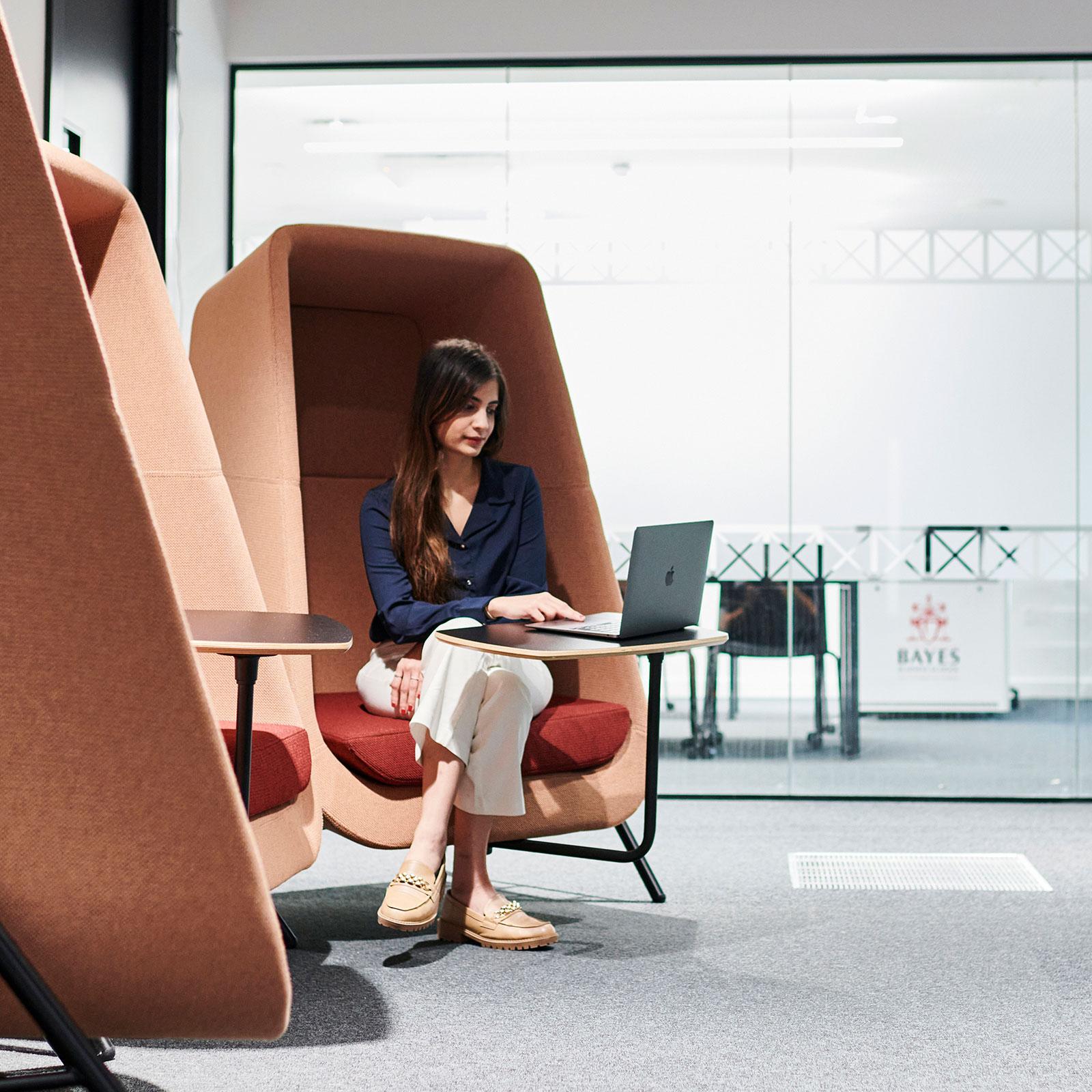 Young woman working on a laptop, seated in a pod chair in Finsbury Square building.