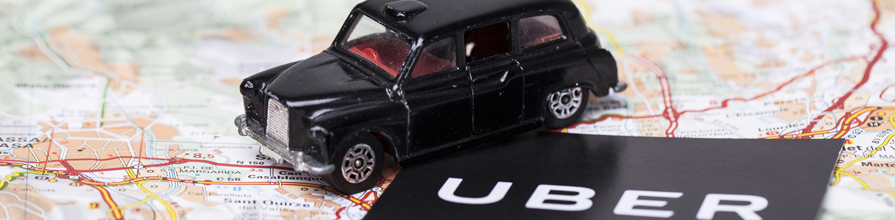 Black taxi toy next to Uber logo on a map