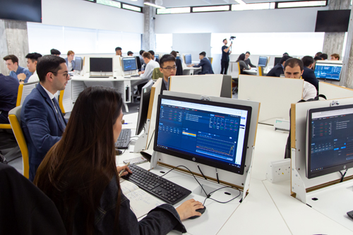 students sit around computer screens showing financial graphs
