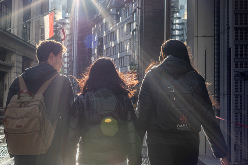 Back of three students walking next to each other, sunshine shining on the students
