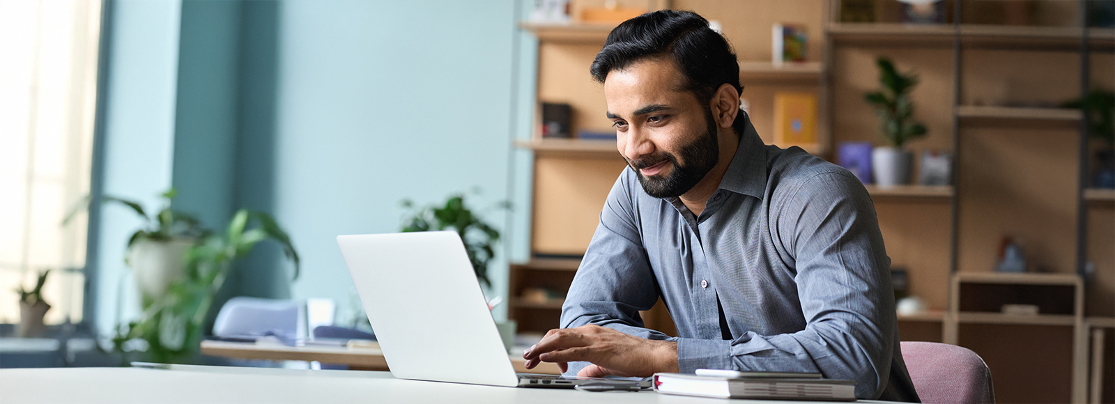 Smiling young Indian man working on a laptop at home.