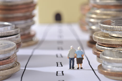 A miniature model of an elderly couple walking on a path between towering piles of coins