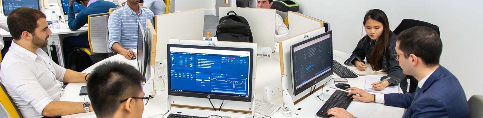 students sit around computer screens showing financial graphs