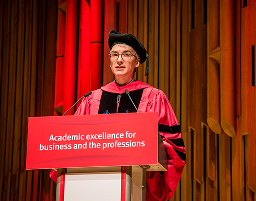 man in red gown and robes stands behind a lectern