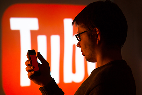 Student looking at phone with YouTube logo on a large screen in the background