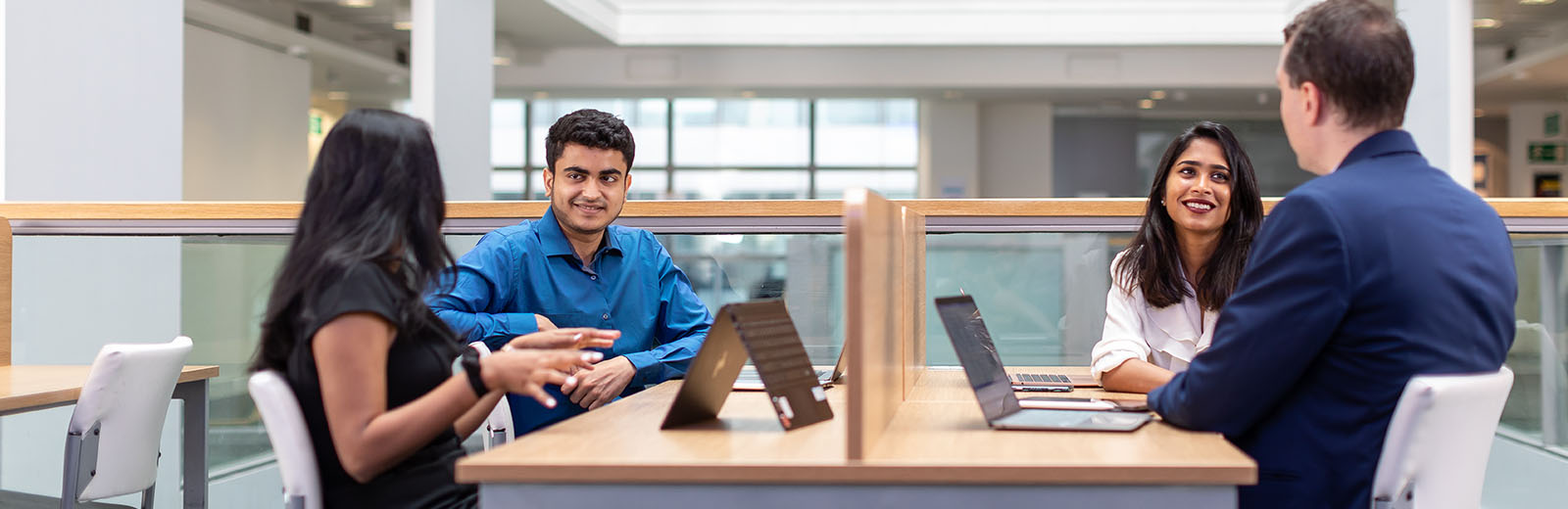 Group of four Bayes students in discussion with laptop 