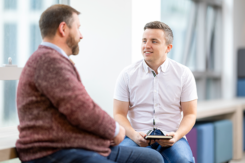 Two men sitting down facing each other talking