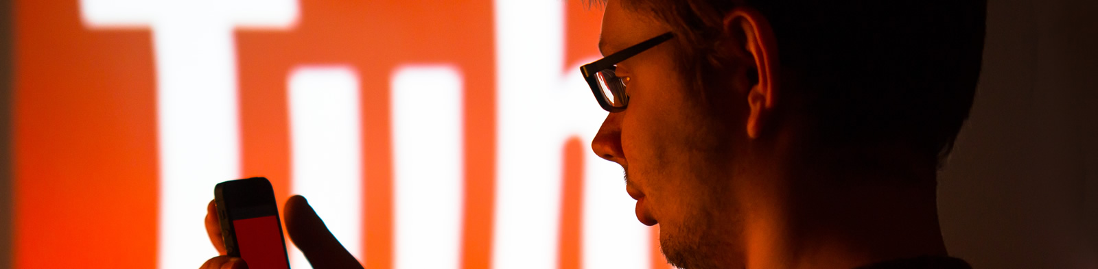 Student looking at phone with YouTube logo on a large screen in the background